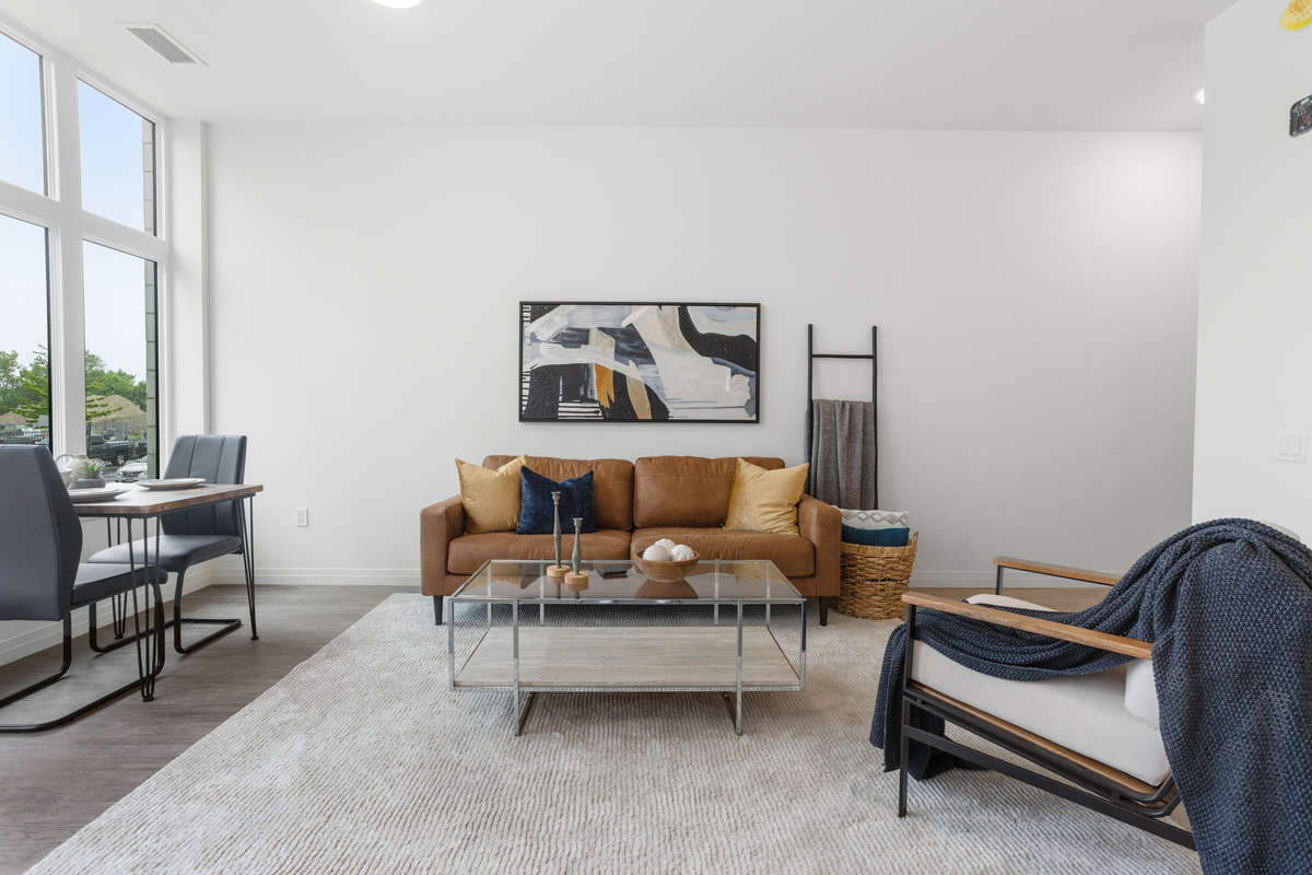 Bright spacious modern open concept living room, w couch, coffee table, armchair and a dining table by a window. Photo of a one-bedroom model suite apartment at Zerin Place on South Street at 370 South St. in London Ontario. A housing project by Zerin Development in VillageSoHo.